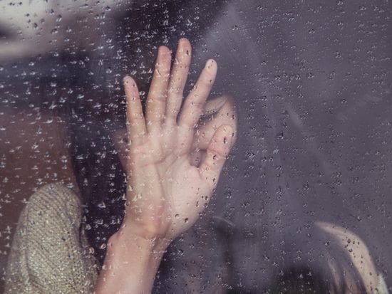 woman with hand up against rainy window