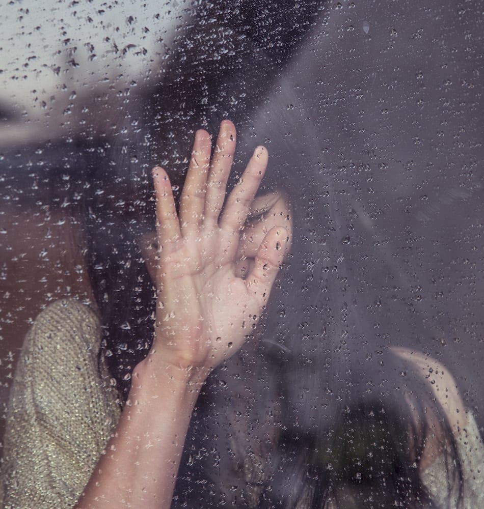 woman with hand up against rainy window