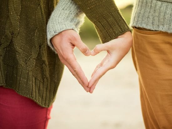 two women in sweaters with their hands shaping into a heart
