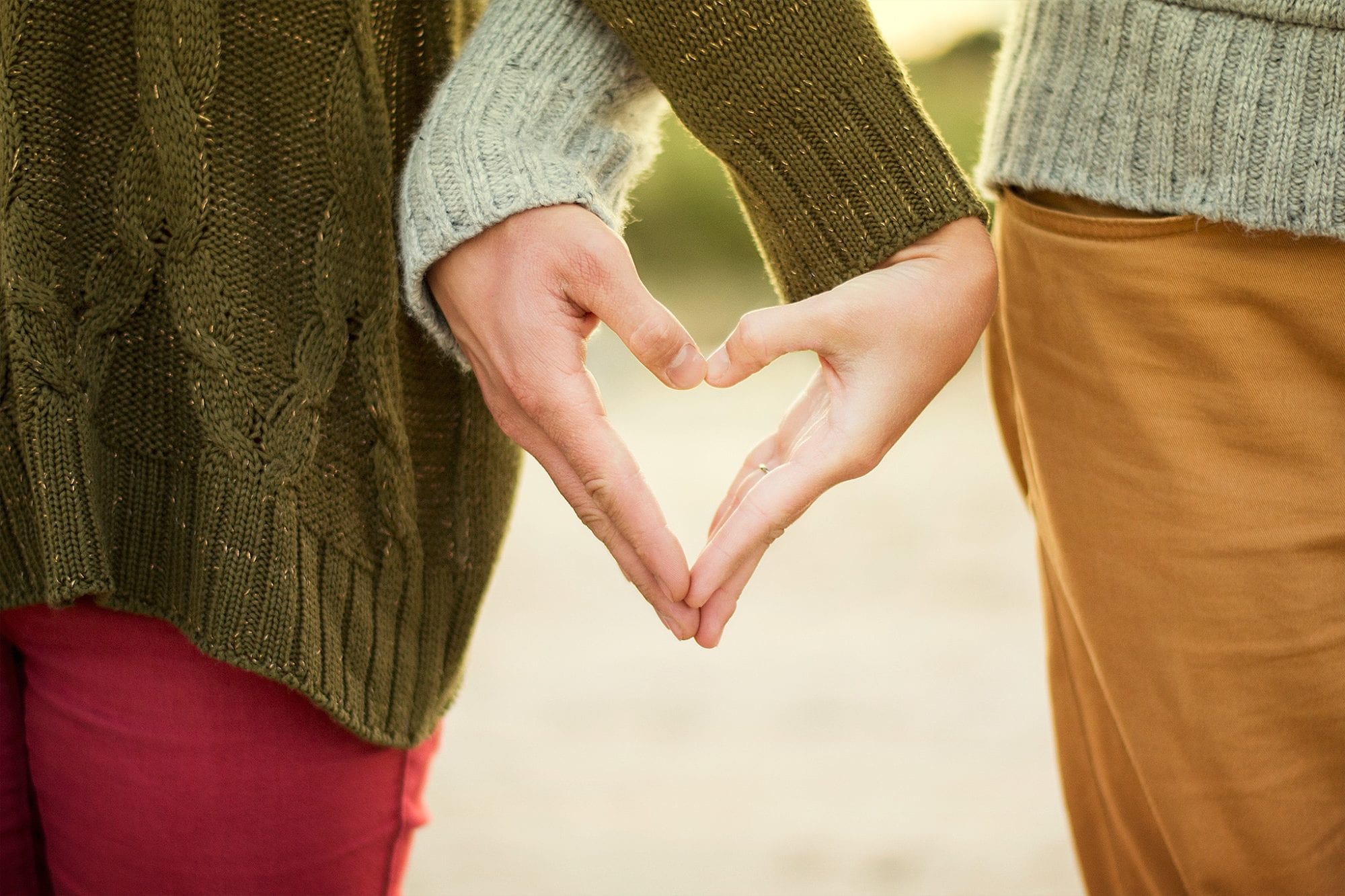 two women in sweaters with their hands shaping into a heart