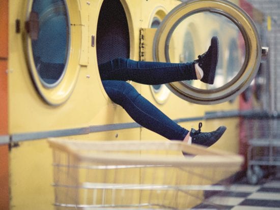 woman's legs sticking out of a dryer at the laundromat