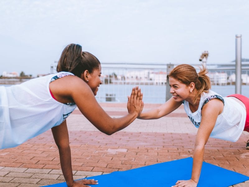 two african American women doing pushups and high fiving outdoors