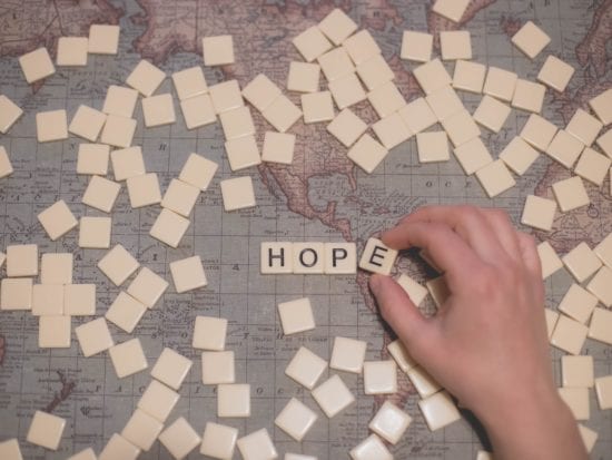 a hand playing with scrabbble tiles on a map with the word HOPE