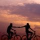 keeping the spark alive - young couple biking in a sunset holding hands